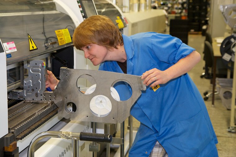 Employée en blouse bleue de production réglant une pièce sur une machine d'assemblage de composants électroniques dans une usine allemande